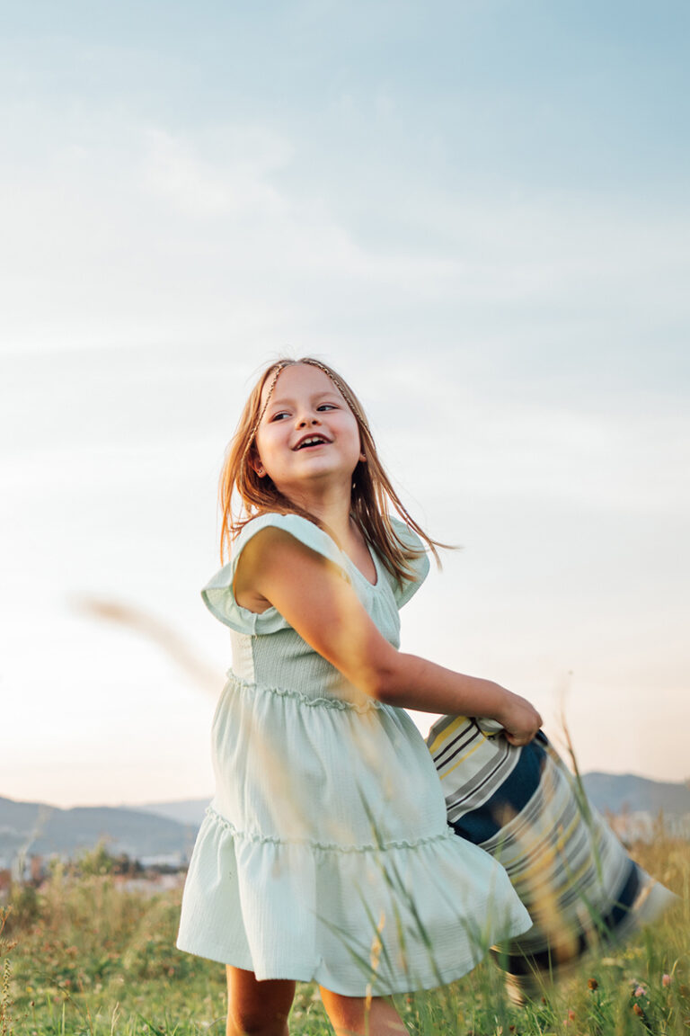 Two laughing sisters have pillow fight on green grass meadow while they have outdoor natural walking in evening. Family values concept image.
